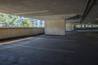 an empty parking lot with a concrete wall and trees in the background and buildings on both sides