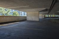 an empty parking lot with a concrete wall and trees in the background and buildings on both sides