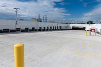 an empty parking lot with many yellow caution poles near a factory building and lots of trucks