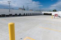 an empty parking lot with many yellow caution poles near a factory building and lots of trucks