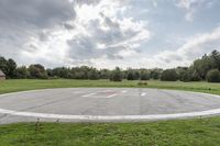 a empty parking lot with no one on the grass outside, a large circular basketball court in the middle of a green field