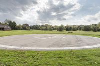 a empty parking lot with no one on the grass outside, a large circular basketball court in the middle of a green field