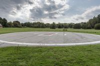 a empty parking lot with no one on the grass outside, a large circular basketball court in the middle of a green field