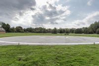 a empty parking lot with no one on the grass outside, a large circular basketball court in the middle of a green field