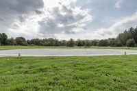 a empty parking lot with no one on the grass outside, a large circular basketball court in the middle of a green field