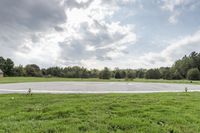 a empty parking lot with no one on the grass outside, a large circular basketball court in the middle of a green field