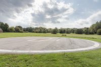 a empty parking lot with no one on the grass outside, a large circular basketball court in the middle of a green field