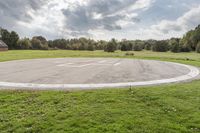 a empty parking lot with no one on the grass outside, a large circular basketball court in the middle of a green field