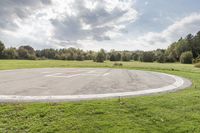 a empty parking lot with no one on the grass outside, a large circular basketball court in the middle of a green field