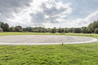 a empty parking lot with no one on the grass outside, a large circular basketball court in the middle of a green field