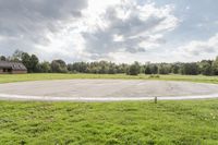 a empty parking lot with no one on the grass outside, a large circular basketball court in the middle of a green field