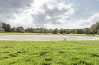 a empty parking lot with no one on the grass outside, a large circular basketball court in the middle of a green field