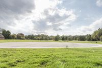 a empty parking lot with no one on the grass outside, a large circular basketball court in the middle of a green field