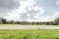 a empty parking lot with no one on the grass outside, a large circular basketball court in the middle of a green field