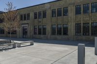 the empty parking lot outside of a brick building has benches and trees on it and trees around