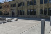 the empty parking lot outside of a brick building has benches and trees on it and trees around