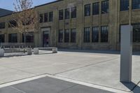 the empty parking lot outside of a brick building has benches and trees on it and trees around