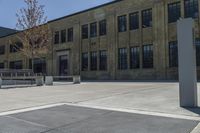 the empty parking lot outside of a brick building has benches and trees on it and trees around