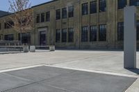 the empty parking lot outside of a brick building has benches and trees on it and trees around