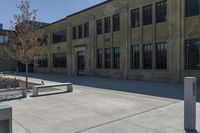 the empty parking lot outside of a brick building has benches and trees on it and trees around