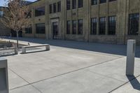 the empty parking lot outside of a brick building has benches and trees on it and trees around