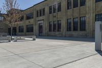 the empty parking lot outside of a brick building has benches and trees on it and trees around