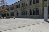 the empty parking lot outside of a brick building has benches and trees on it and trees around