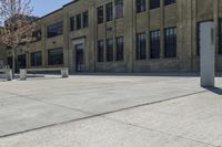 the empty parking lot outside of a brick building has benches and trees on it and trees around