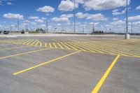 an empty parking lot with yellow markings on the ground beneath clouds in blue skys