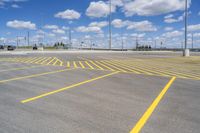 an empty parking lot with yellow markings on the ground beneath clouds in blue skys