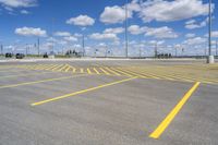 an empty parking lot with yellow markings on the ground beneath clouds in blue skys