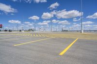 an empty parking lot with yellow markings on the ground beneath clouds in blue skys