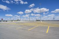 an empty parking lot with yellow markings on the ground beneath clouds in blue skys