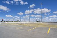 an empty parking lot with yellow markings on the ground beneath clouds in blue skys