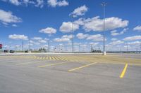 an empty parking lot with yellow markings on the ground beneath clouds in blue skys