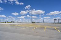 an empty parking lot with yellow markings on the ground beneath clouds in blue skys