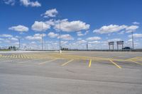 an empty parking lot with yellow markings on the ground beneath clouds in blue skys