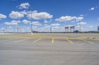 an empty parking lot with yellow markings on the ground beneath clouds in blue skys