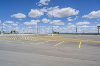 an empty parking lot with yellow markings on the ground beneath clouds in blue skys