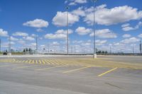 an empty parking lot with yellow markings on the ground beneath clouds in blue skys