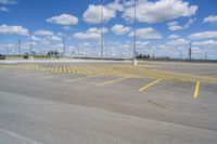 an empty parking lot with yellow markings on the ground beneath clouds in blue skys