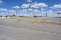 an empty parking lot with yellow markings on the ground beneath clouds in blue skys