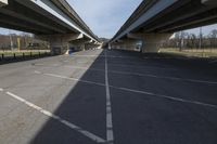 a very empty parking lot beneath an overpass with two cars going under it in the afternoon