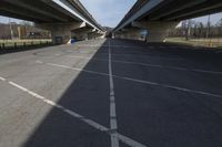 a very empty parking lot beneath an overpass with two cars going under it in the afternoon