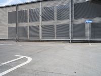 an empty parking lot near a building with several windows on it and a blue traffic sign