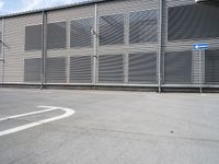 an empty parking lot near a building with several windows on it and a blue traffic sign