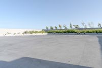 an empty parking lot in front of a building next to a field of grass and bushes