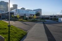 an empty parking lot surrounded by tall buildings and green grass in front of it, surrounded by two rows of trees