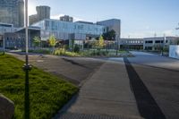 an empty parking lot surrounded by tall buildings and green grass in front of it, surrounded by two rows of trees