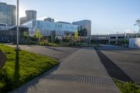 an empty parking lot surrounded by tall buildings and green grass in front of it, surrounded by two rows of trees